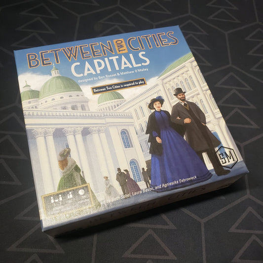 Image shows the front cover of the box of the Capitals expansion for the board game Between Two Cities