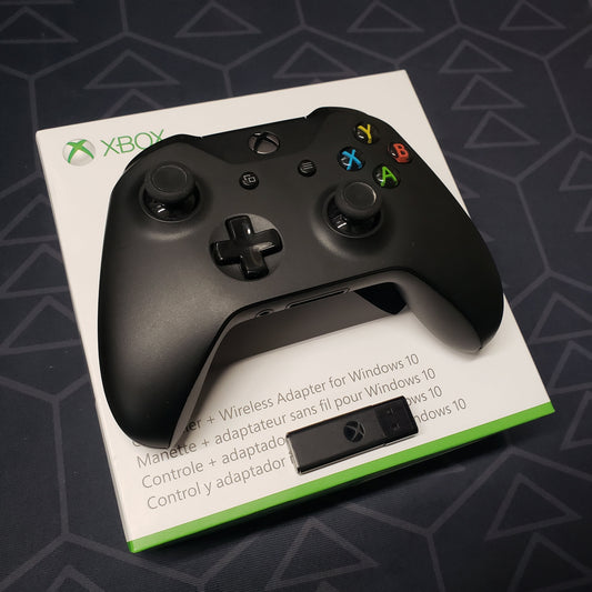 Image shows a black wireless Xbox One gaming controller with a Windows 10 Wireless USB Adapter sitting on top its original box