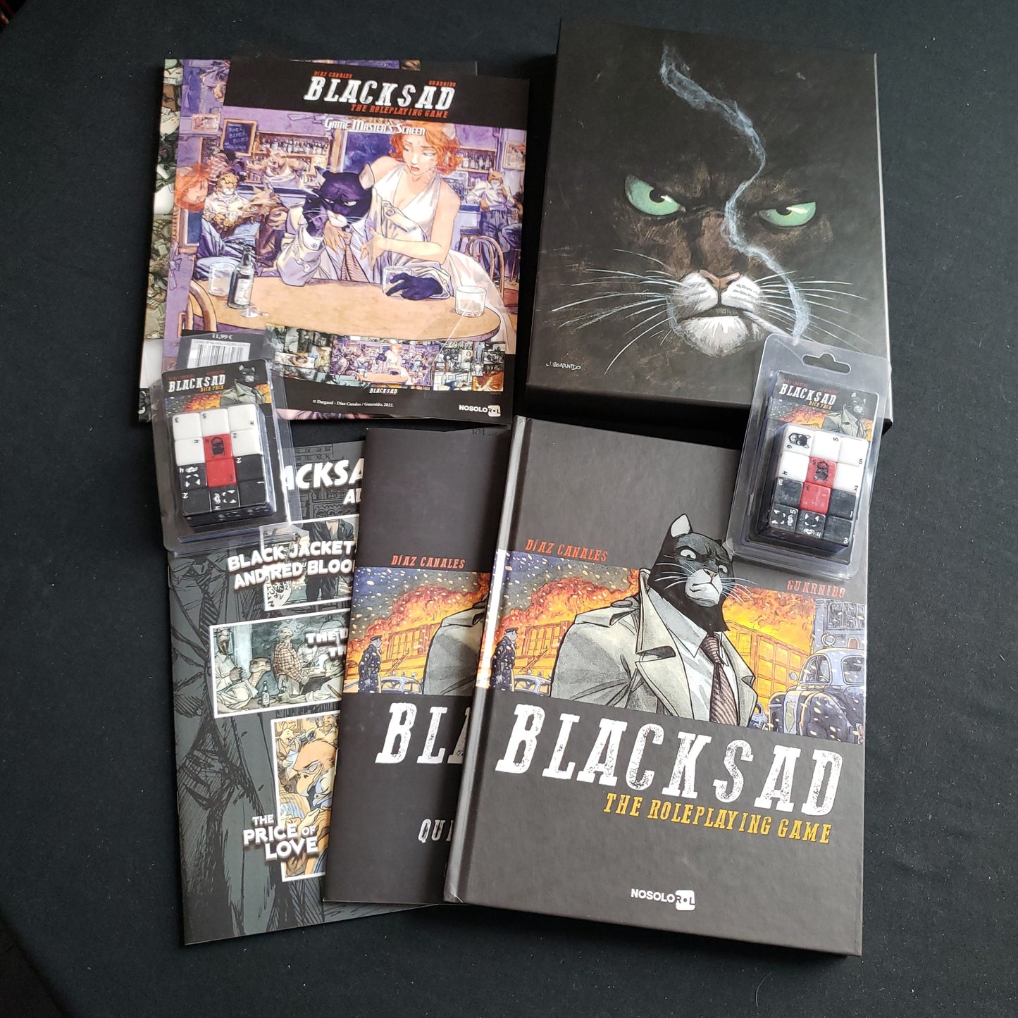 Image shows the books & components from the True Detective Kickstarter pledge level for Blacksad: The Roleplaying Game fanned out on a table