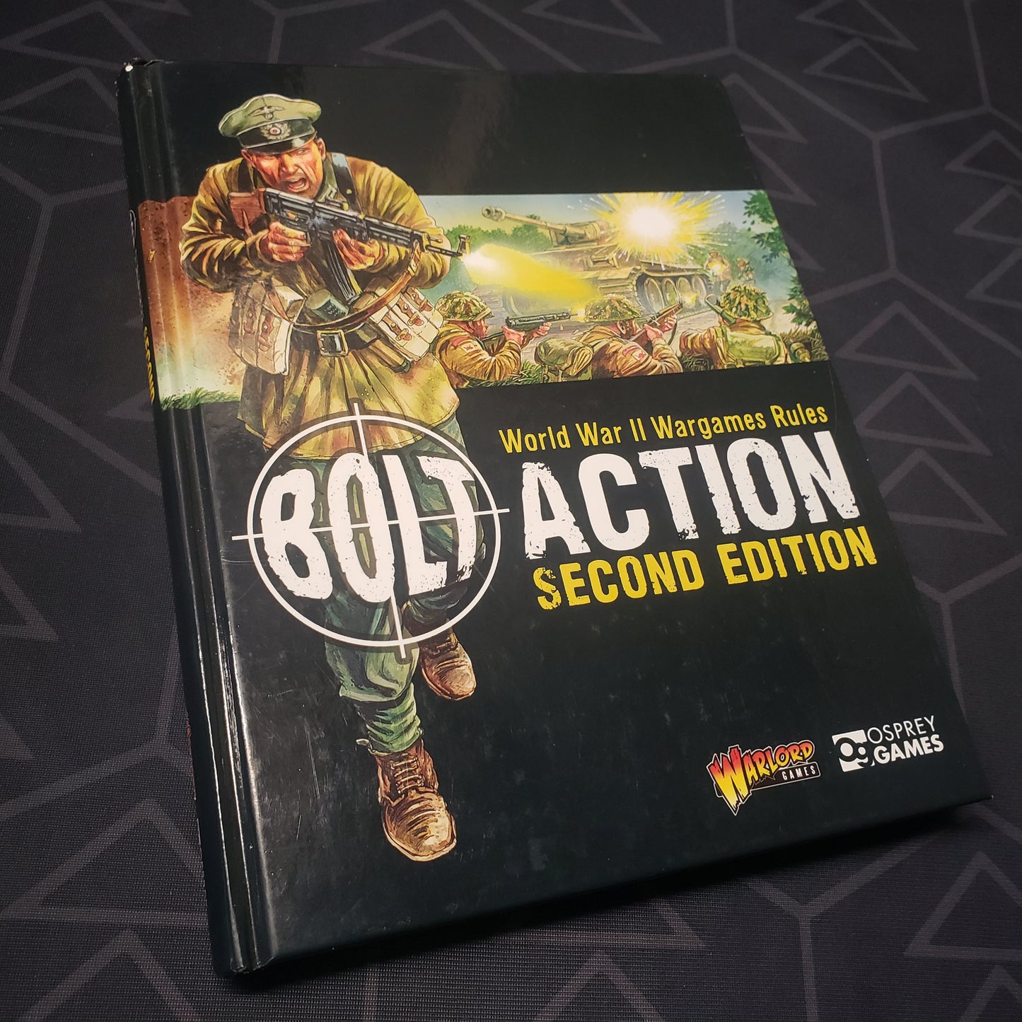 Image shows the front cover of the second edition core rulebook for the miniatures wargame Bolt Action