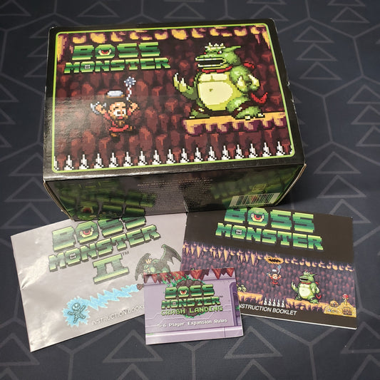 Image shows the front cover of the box of the Collector Box for the card game Boss Monster, surrounded by instruction manuals