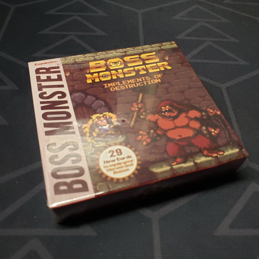 Image shows the front cover of the box of the Implements of Destruction expansion for the card game Boss Monster