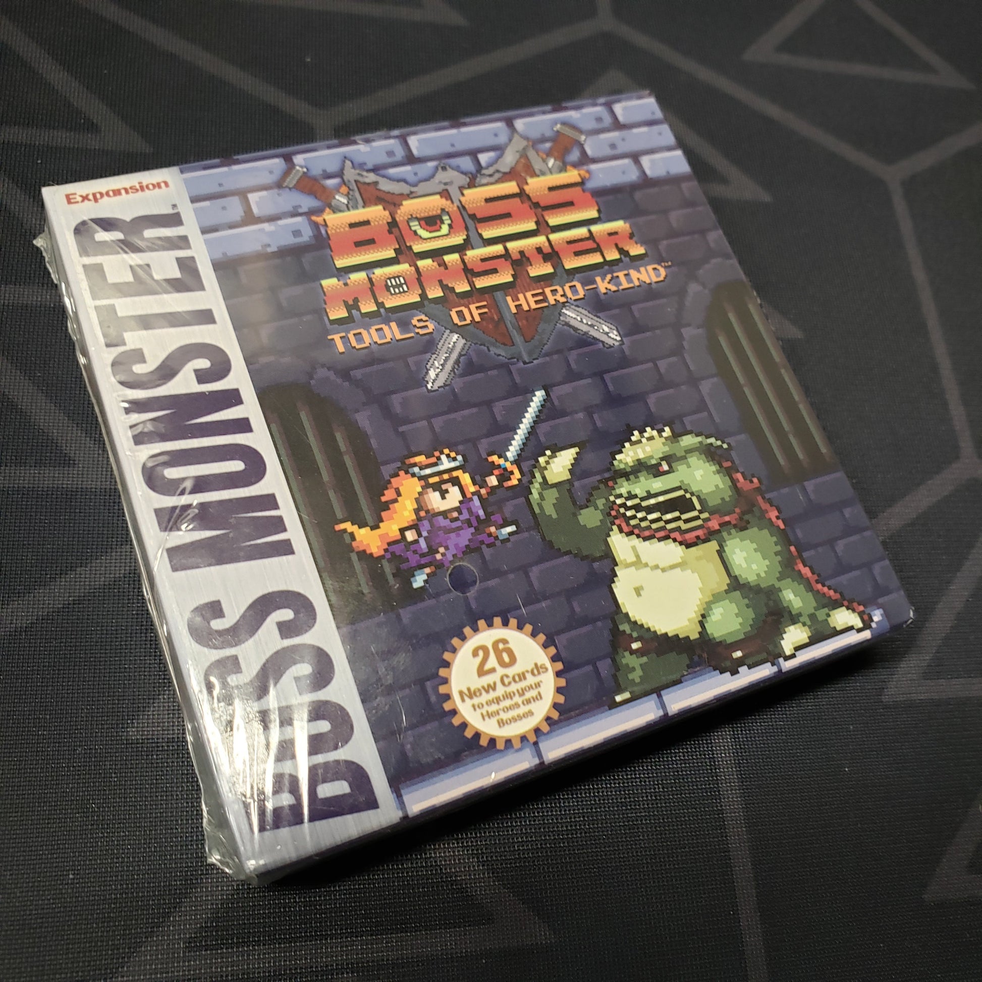 Image shows the front cover of the Tools of Hero Kind expansion for the card game Boss Monster
