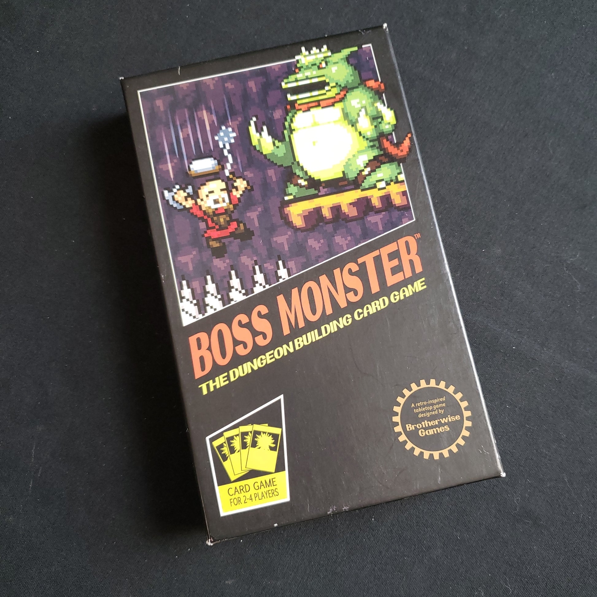 Image shows the front cover of the box of the Boss Monster card game