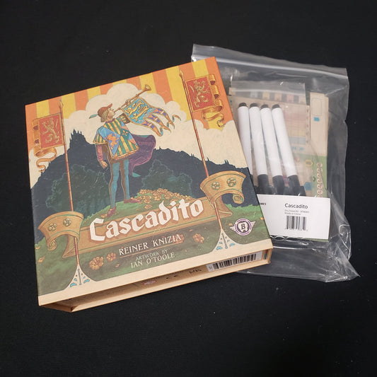 Image shows the front cover of the box of the Cascadito board game sitting on top of the dry erase boards for it