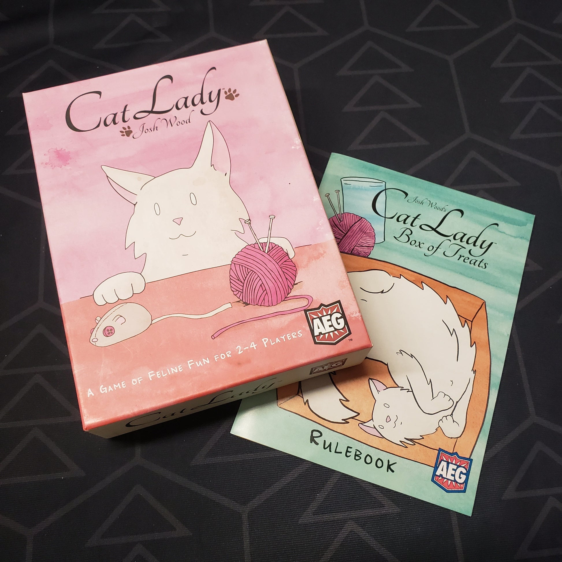 Image shows the front cover of the box for the Cat Lady card game sitting on top of the instructions for the Box of Treats expansion
