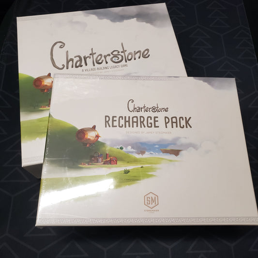 Image shows the front cover of the box for the Charterstone board game with the Recharge Pack for the game sitting on top of it