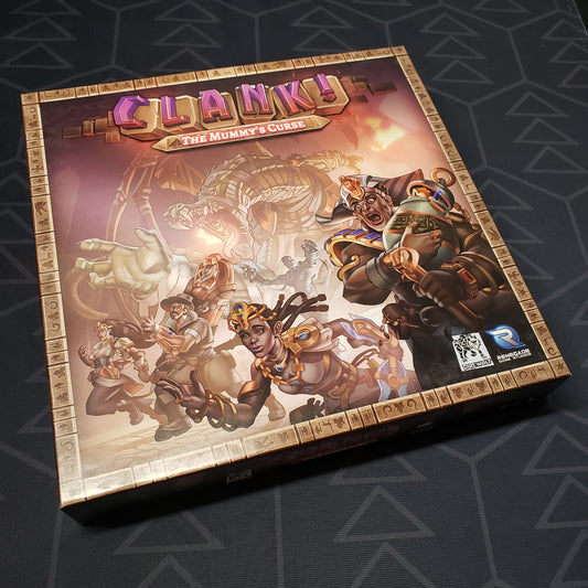 Image shows the front cover of the box of the Mummy's Curse expansion for the board game Clank!