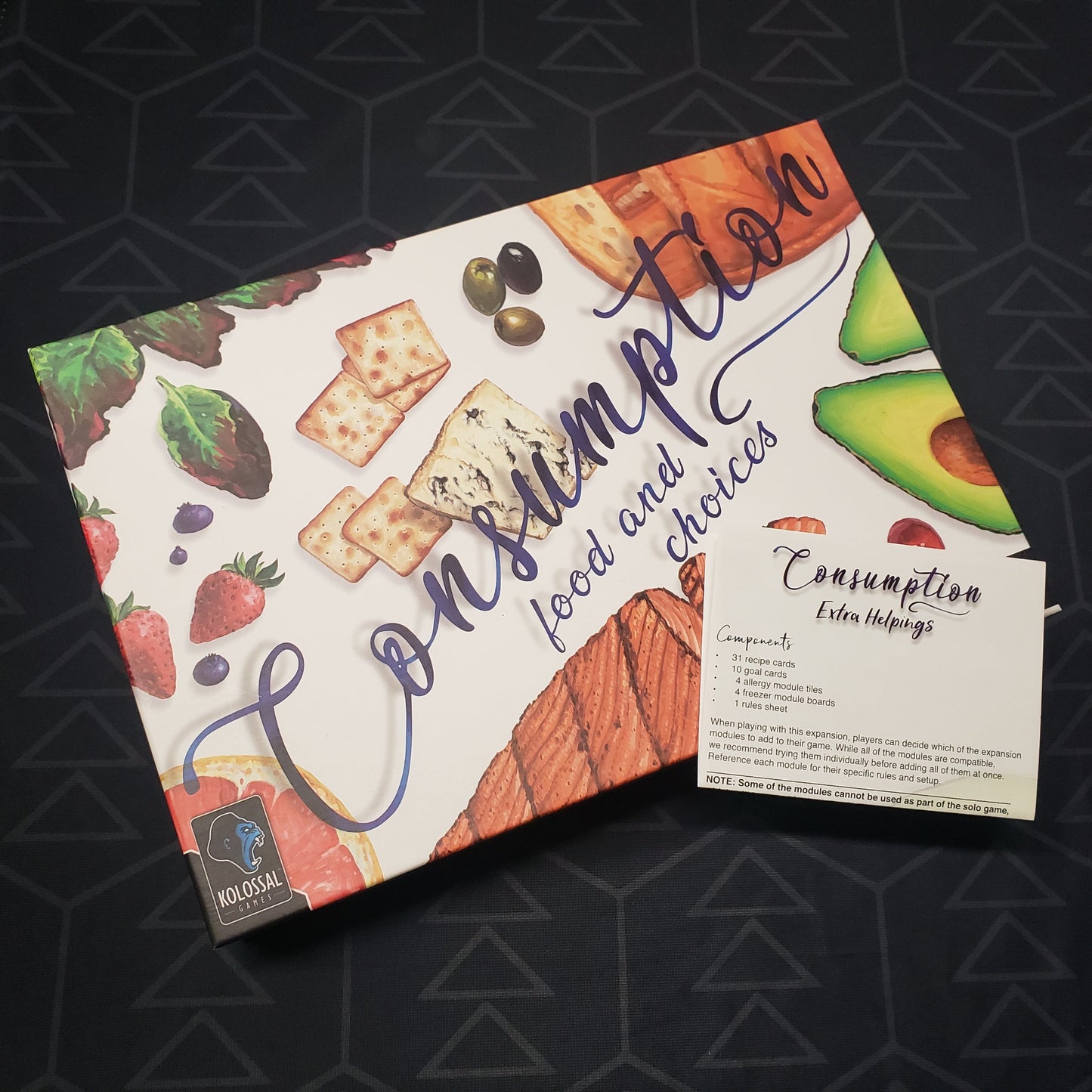Image shows the front cover of the box for the Consumption: Food and Choices board game with the instructions for the Extra Helpings expansion sitting on top of it