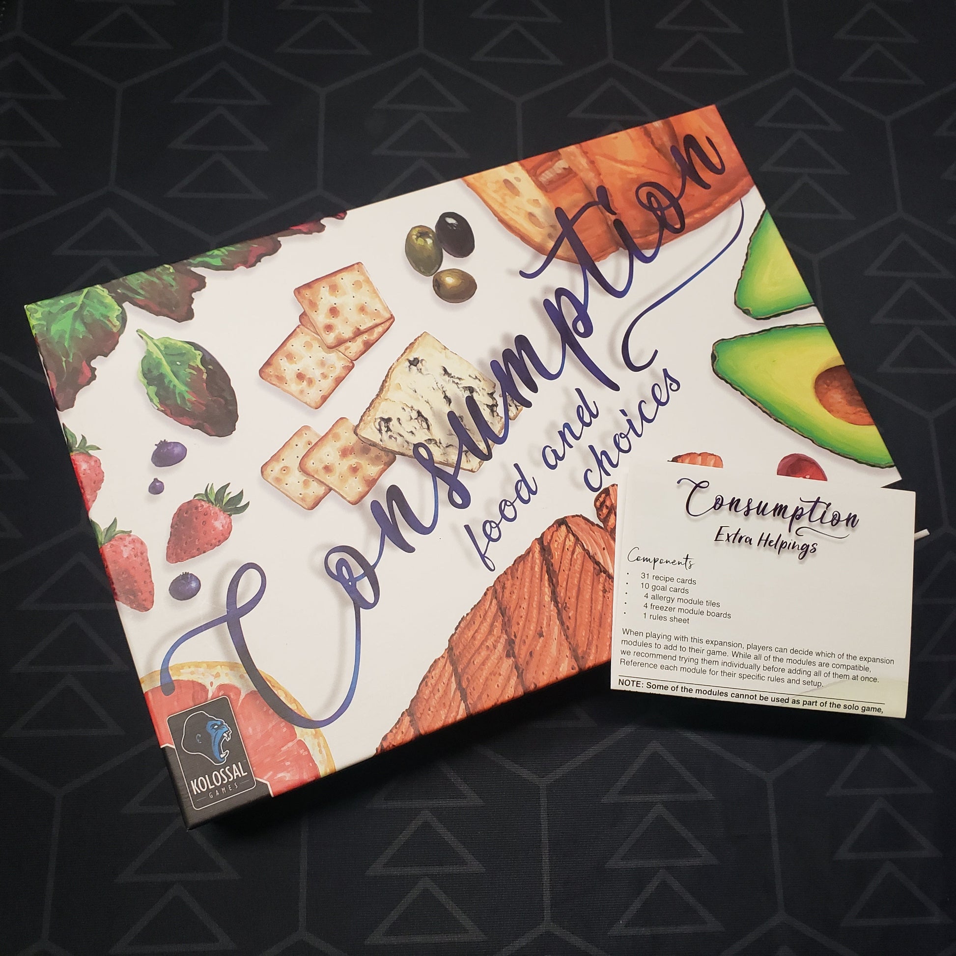 Image shows the front cover of the box for the Consumption: Food and Choices board game with the instructions for the Extra Helpings expansion sitting on top of it