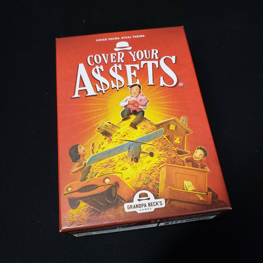 Image shows the front cover of the box of the Cover Your Assets card game