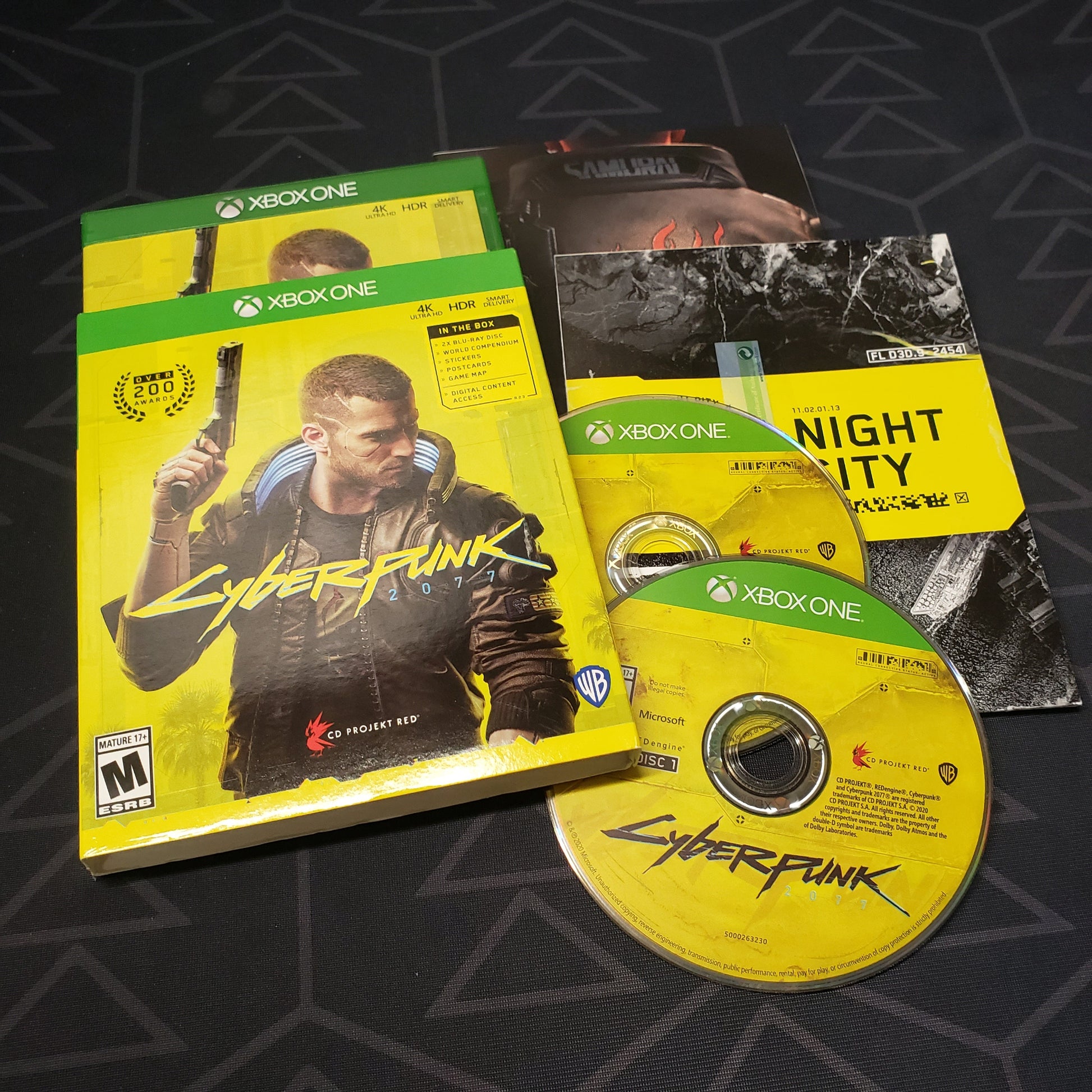 Image shows the case, sleeve, manual, map and two discs for the video game Cyberpunk 2077 for Xbox One