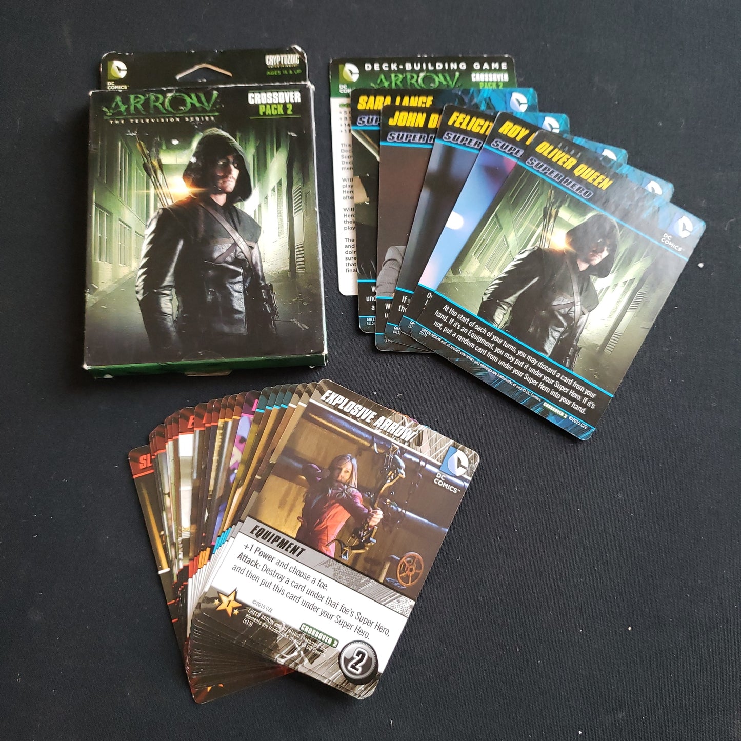 Image shows the front cover of the box of the Arrow Crossover Pack expansion for the DC Comics Deckbuilding card game, along with the cards fanned out next to it