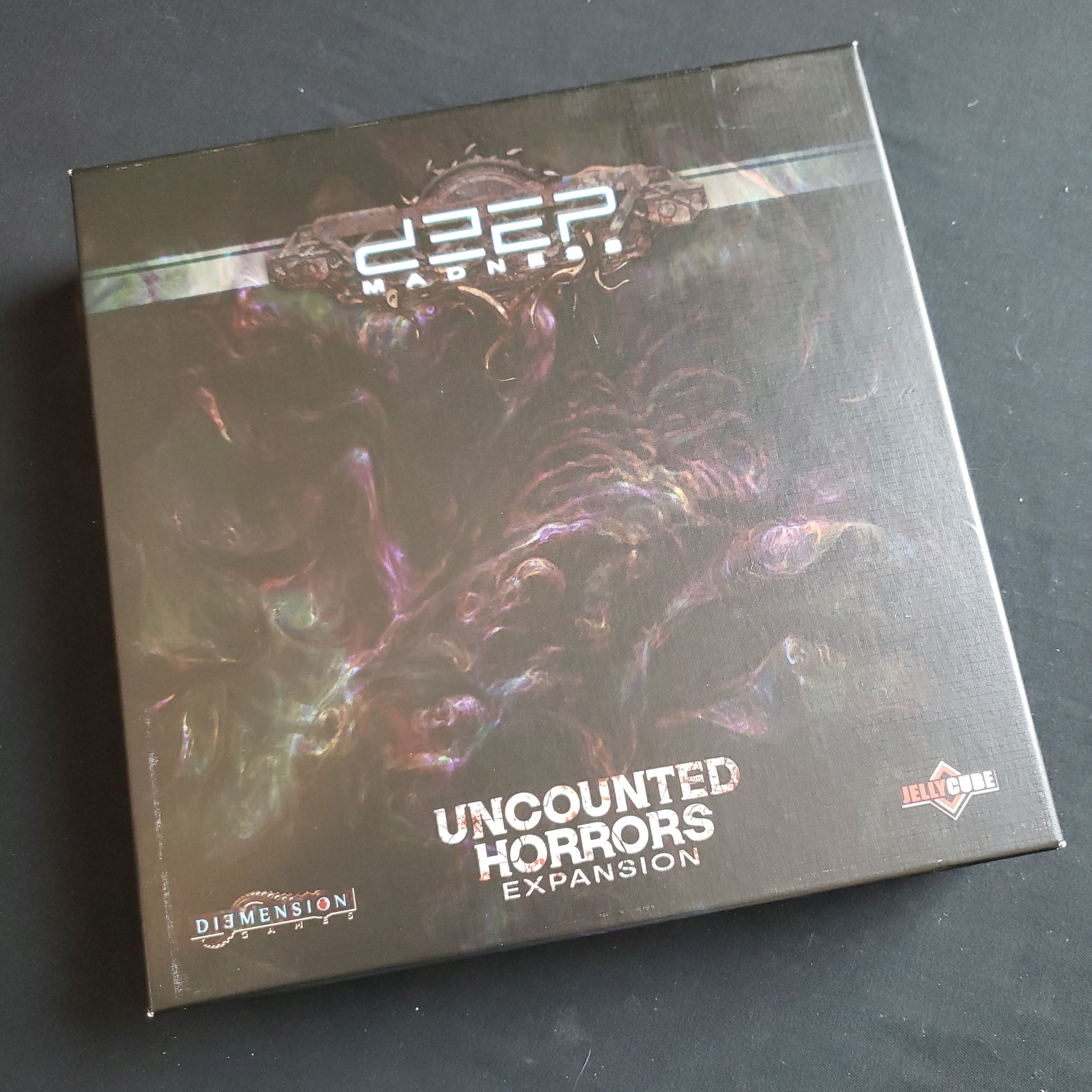 Image shows the front cover of the box of the Uncounted Horrors expansion for the Deep Madness board game
