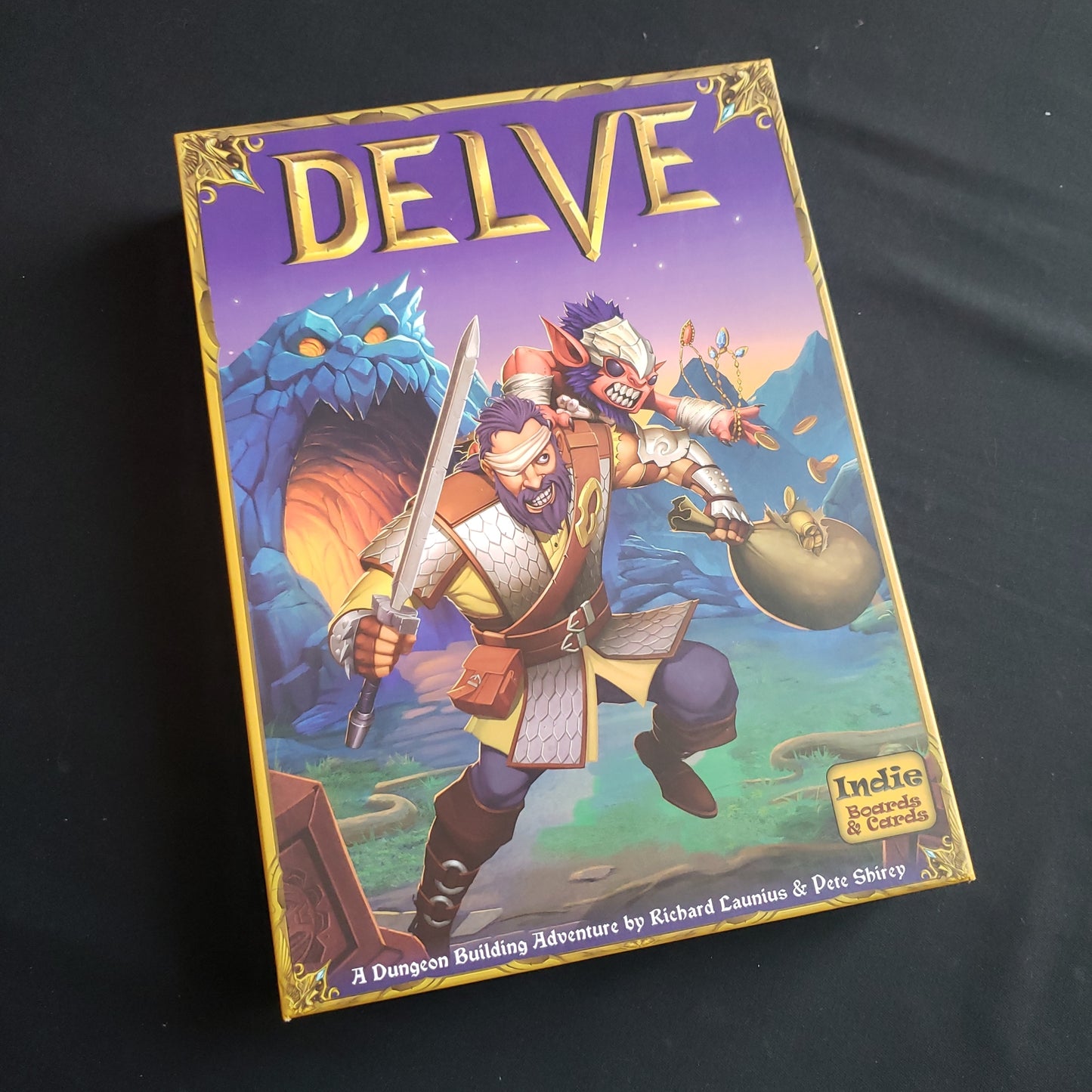 Image shows the front cover of the box of the Delve board game