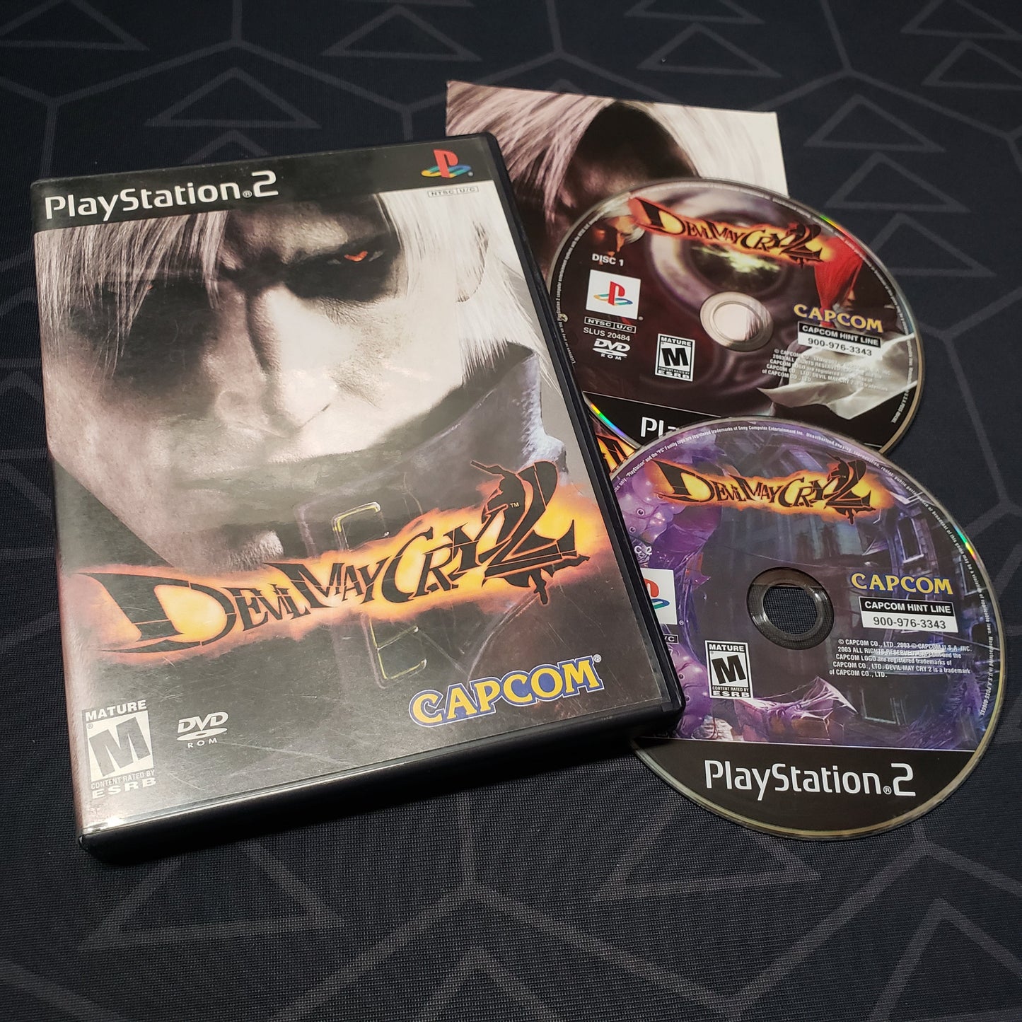 Image shows the case, manual and two discs for the video game Devil May Cry 2 for Playstation 2