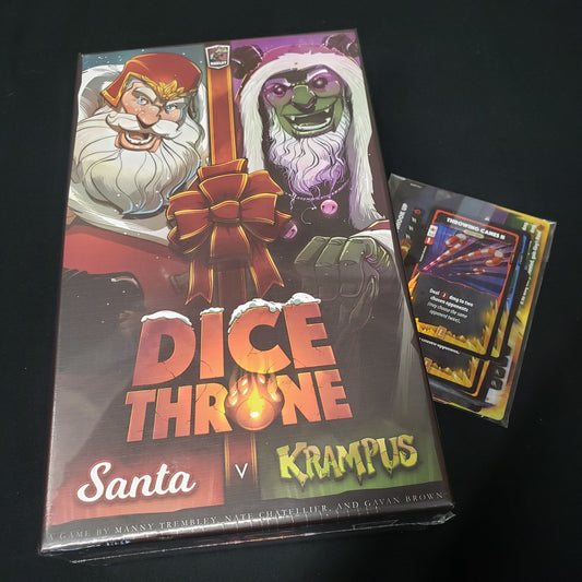 Image shows the front cover of the box of the Dice Throne: Santa v. Krampus board game, sitting on top of a pack of promo cards
