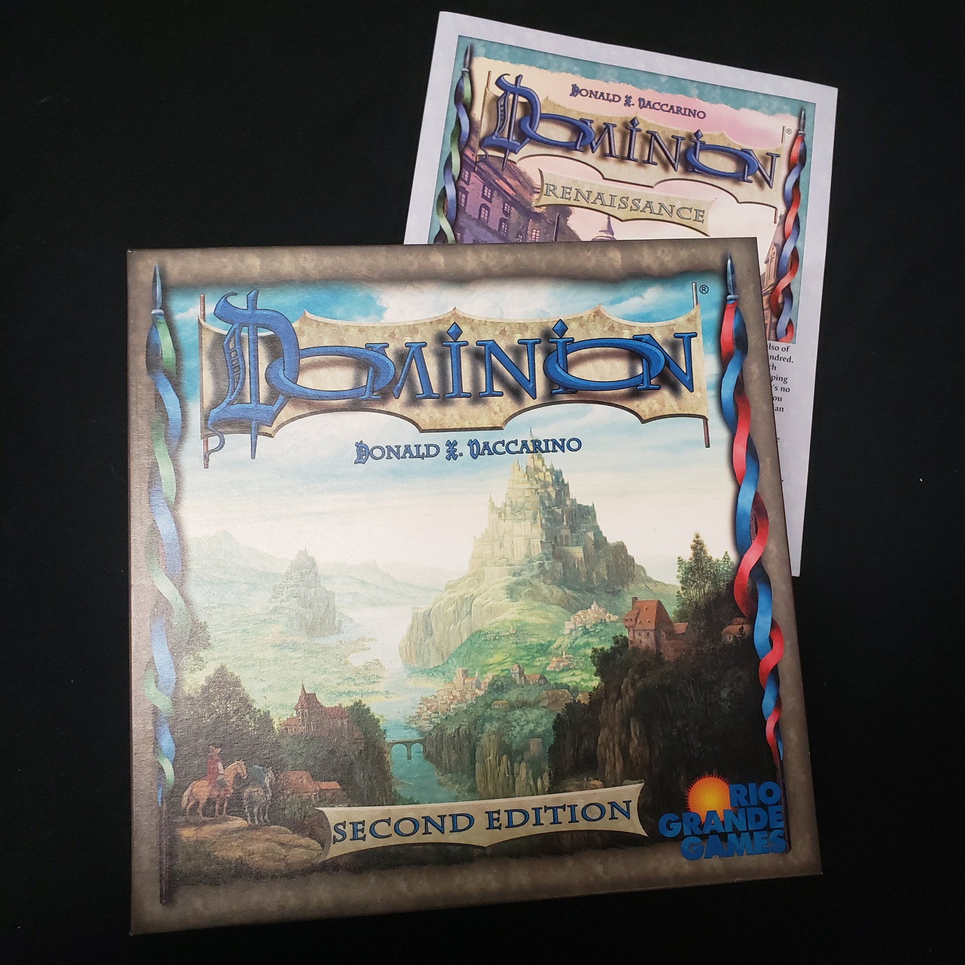 Image shows the front cover of the box of the Dominion card game sitting on top of the instructions for the Renaissance expansion