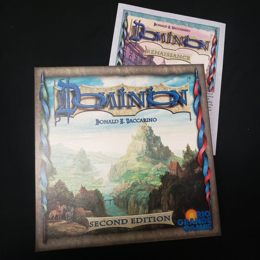 Image shows the front cover of the box of the Dominion card game sitting on top of the instructions for the Renaissance expansion