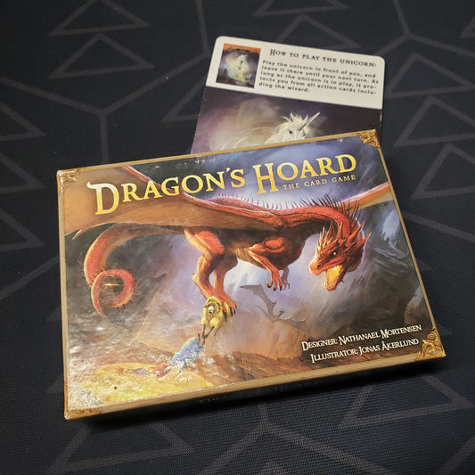 Image shows the front cover of the box for the Dragon's Hoard (First Edition) card game with the Unicorn promo card sitting underneath it