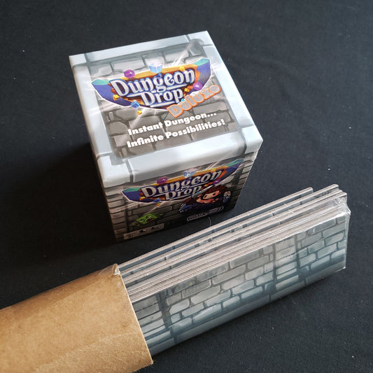 Image shows the top of the box of the Dungeon Drop Deluxe board game, with addition cardboard border pieces in a tube next to it