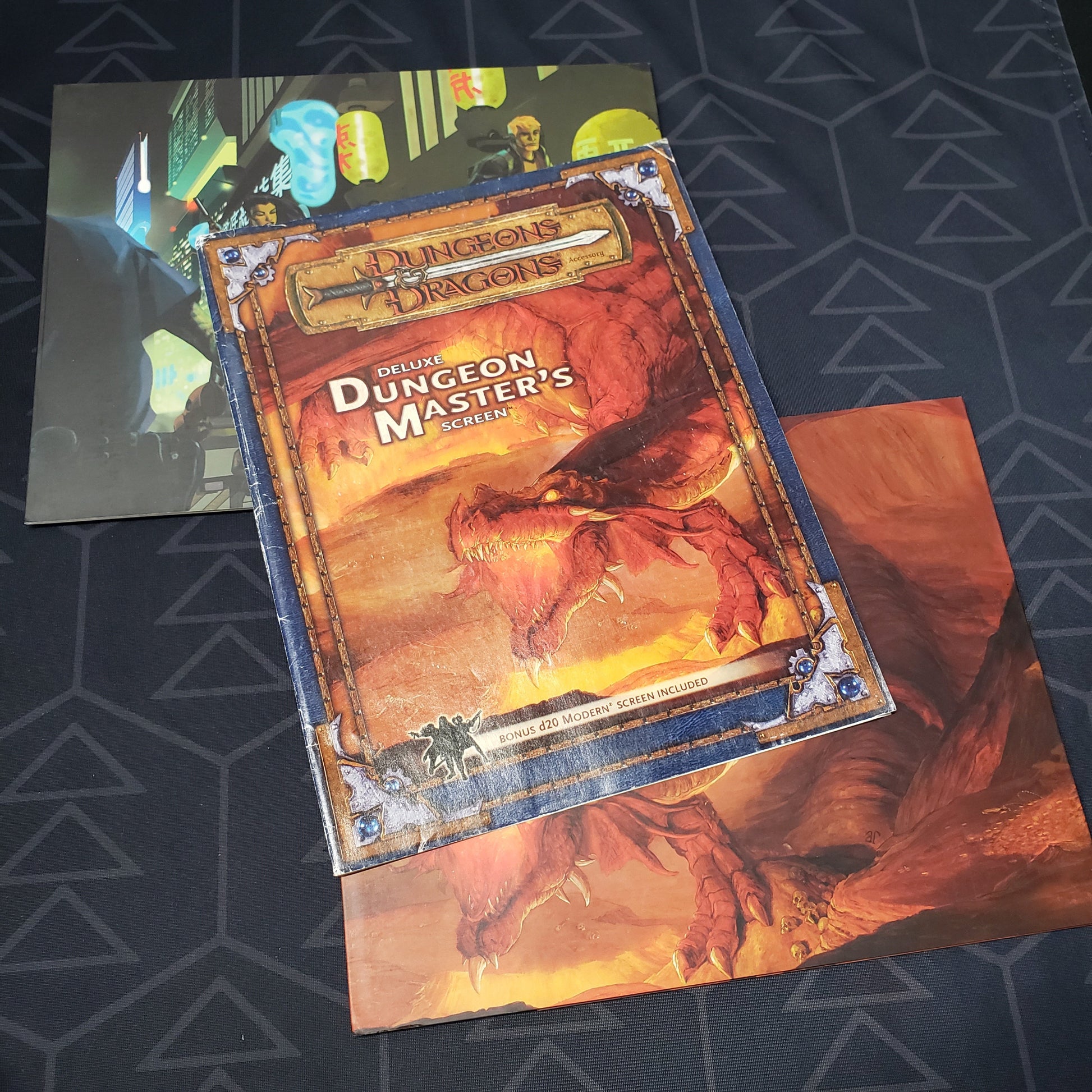 Image shows the front cover and two panels of two different DM screens from the Deluxe Dungeon Master's Screen pack for the roleplaying game Dungeons & Dragons 3.5E