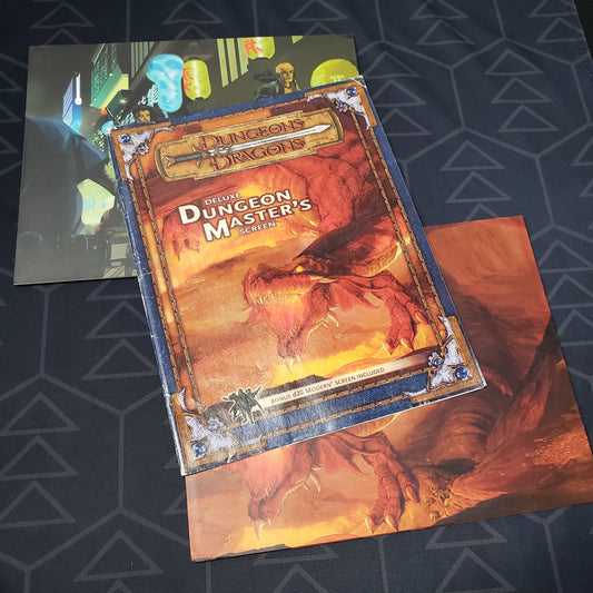 Image shows the front cover and two panels of two different DM screens from the Deluxe Dungeon Master's Screen pack for the roleplaying game Dungeons & Dragons 3.5E
