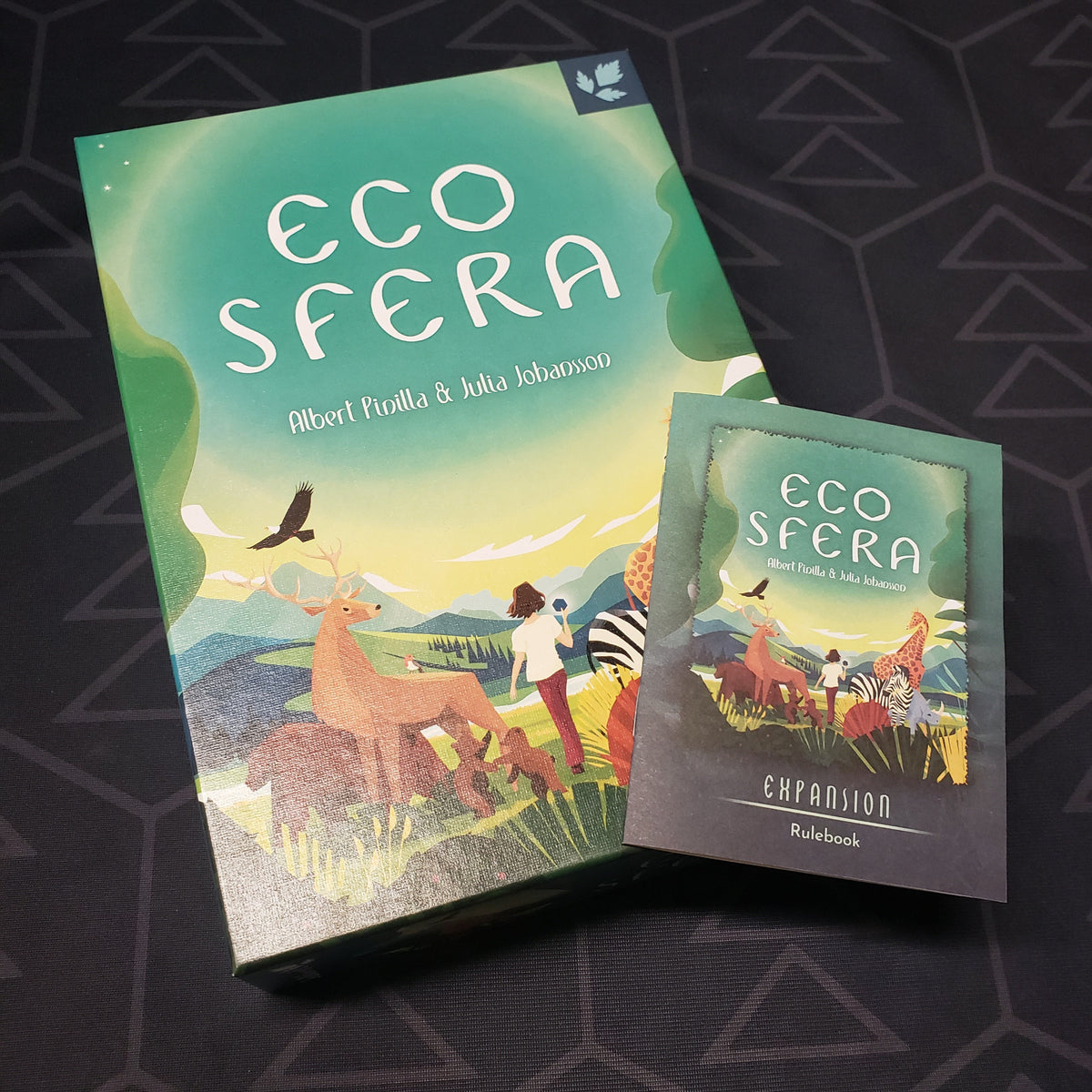 Image shows the front cover of the box for the Ecosfera card game with the expansion instructions sitting on top of it