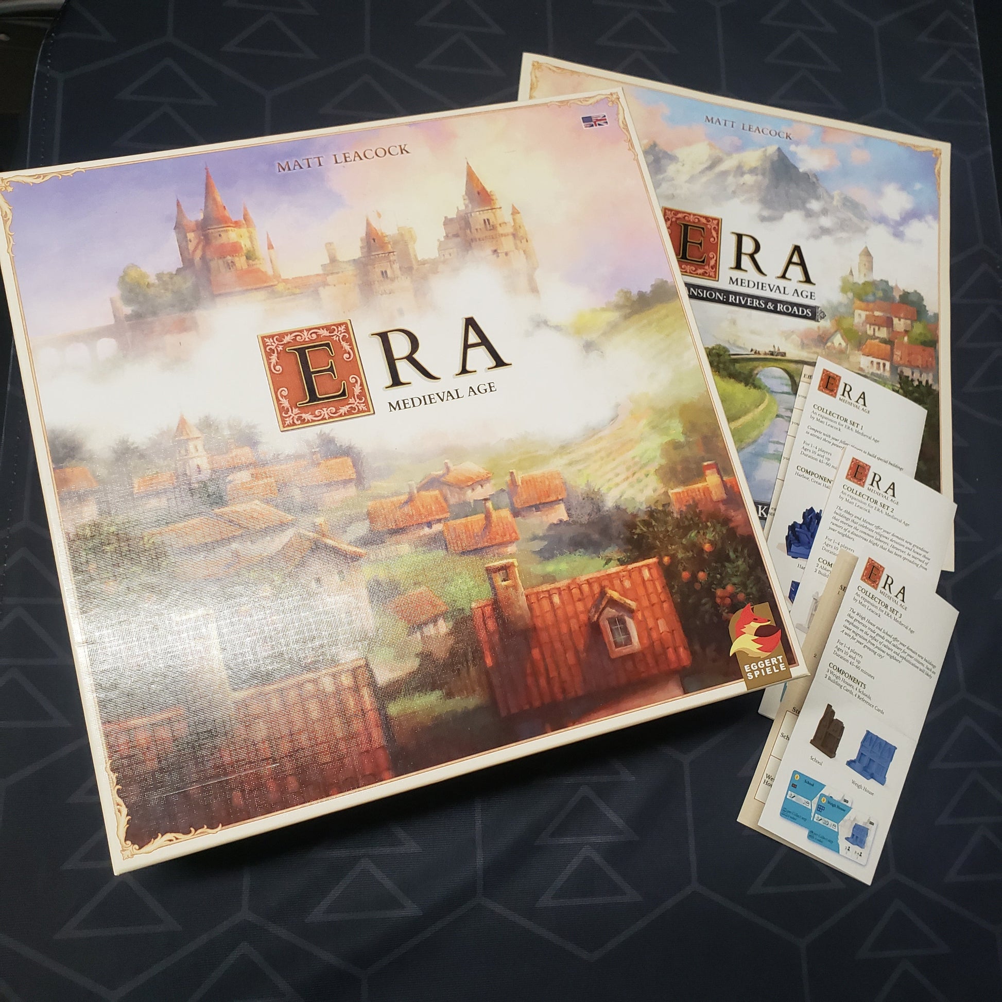 Image shows the front cover of the box for the Era: Medieval Age board game along with several expansion manuals