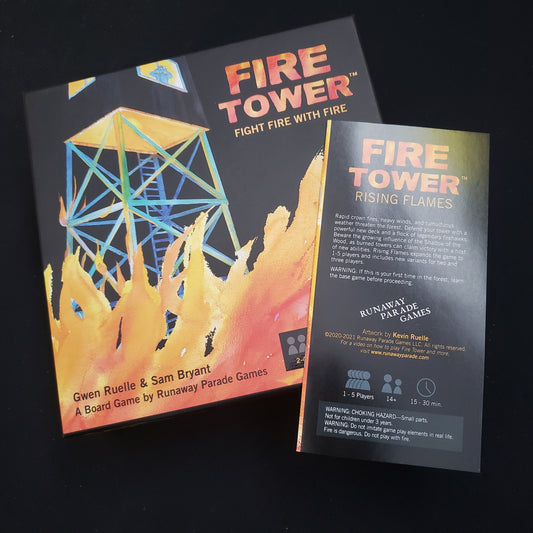 Image shows the front cover of the box of the Fire Tower board game with the instructions for the Rising Flames expansion sitting on top of it