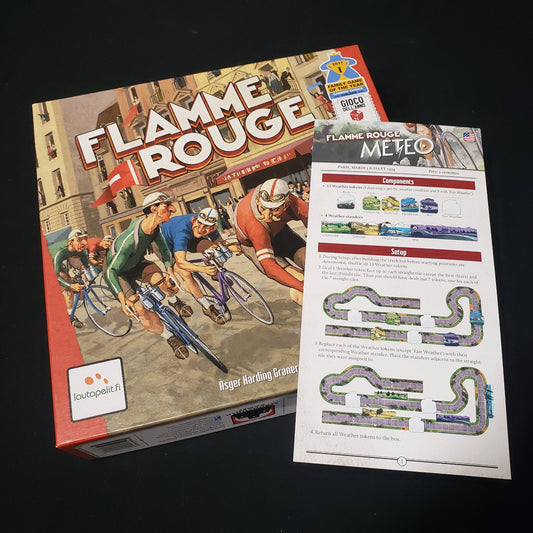 Image shows the front cover of the box of the Flamme Rouge board game with the instructions for the Meteo expansion sitting on top of it