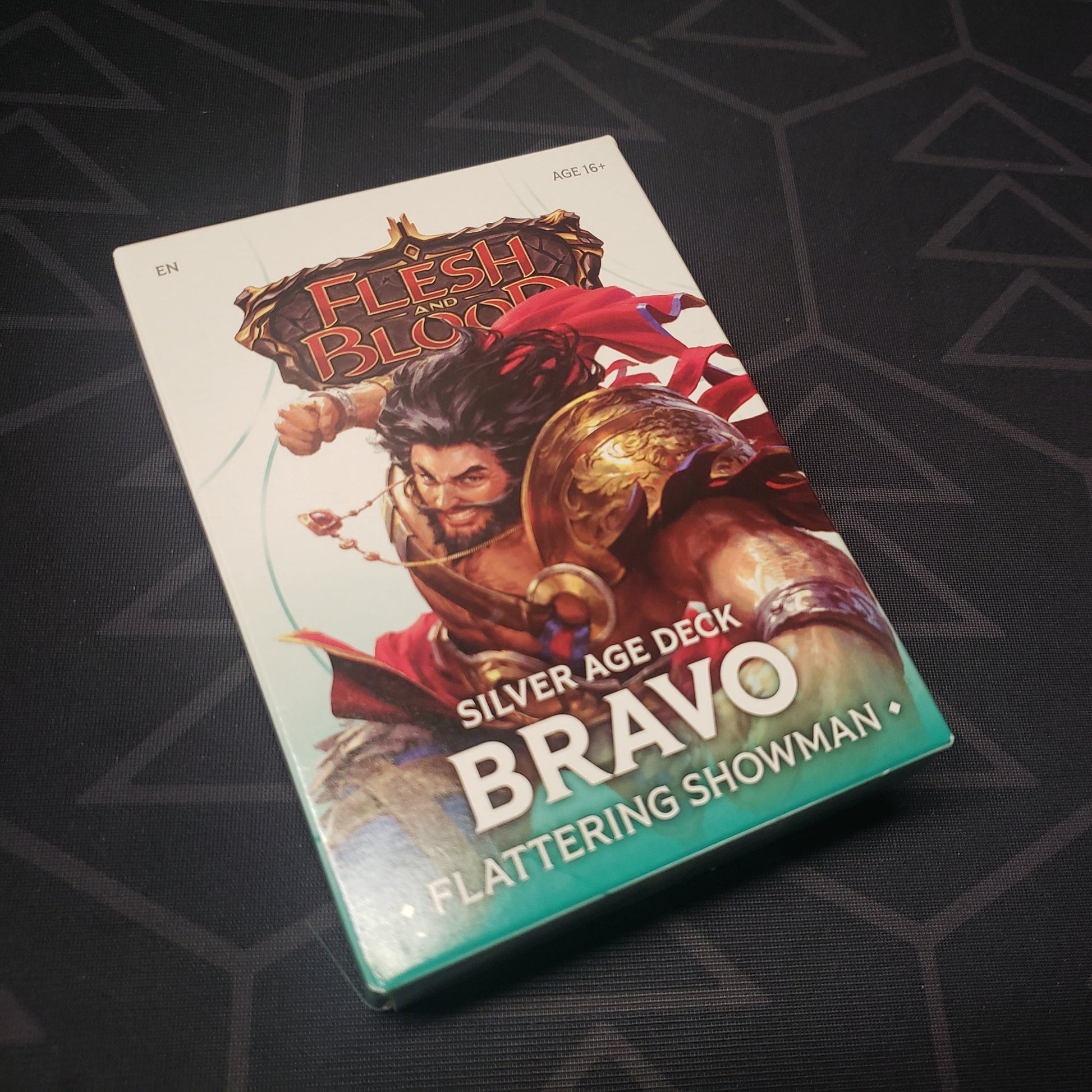 Image shows the front cover of the box of the Silver Age: Bravo, Flattering Showman deck for the card game Flesh & Blood