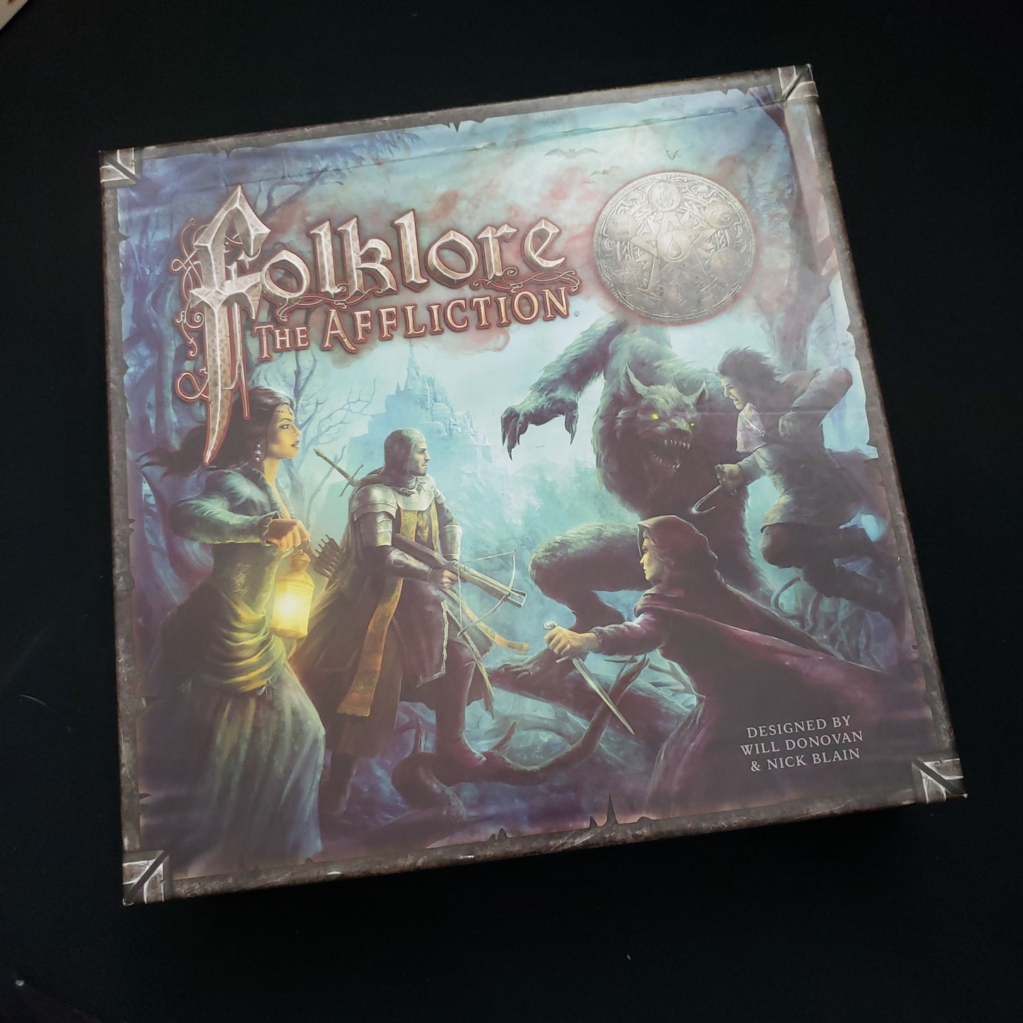 Image shows the front cover of the box of the board game Folklore: The Affliction