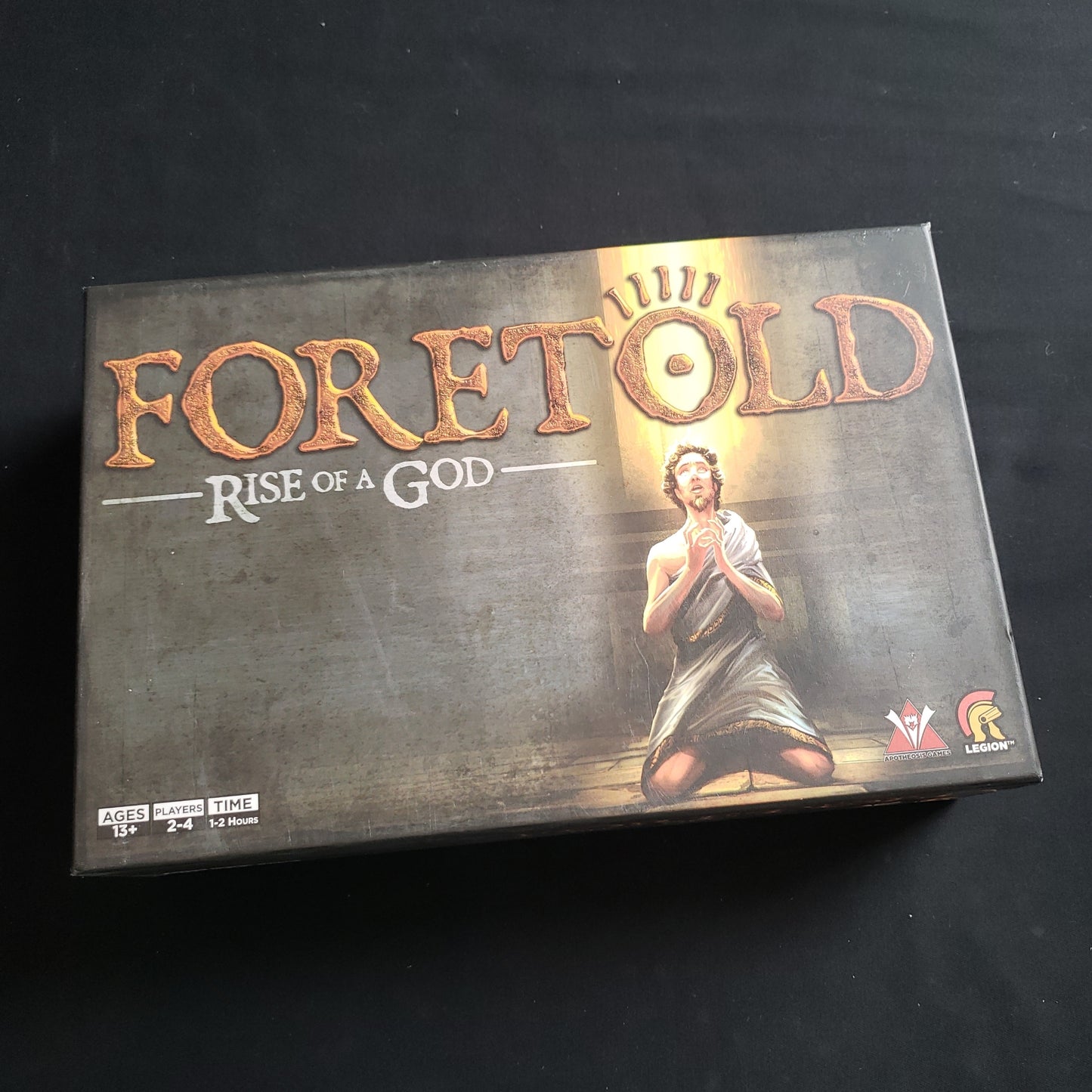 Image shows the front cover of the box of the Foretold: Rise of a God board game