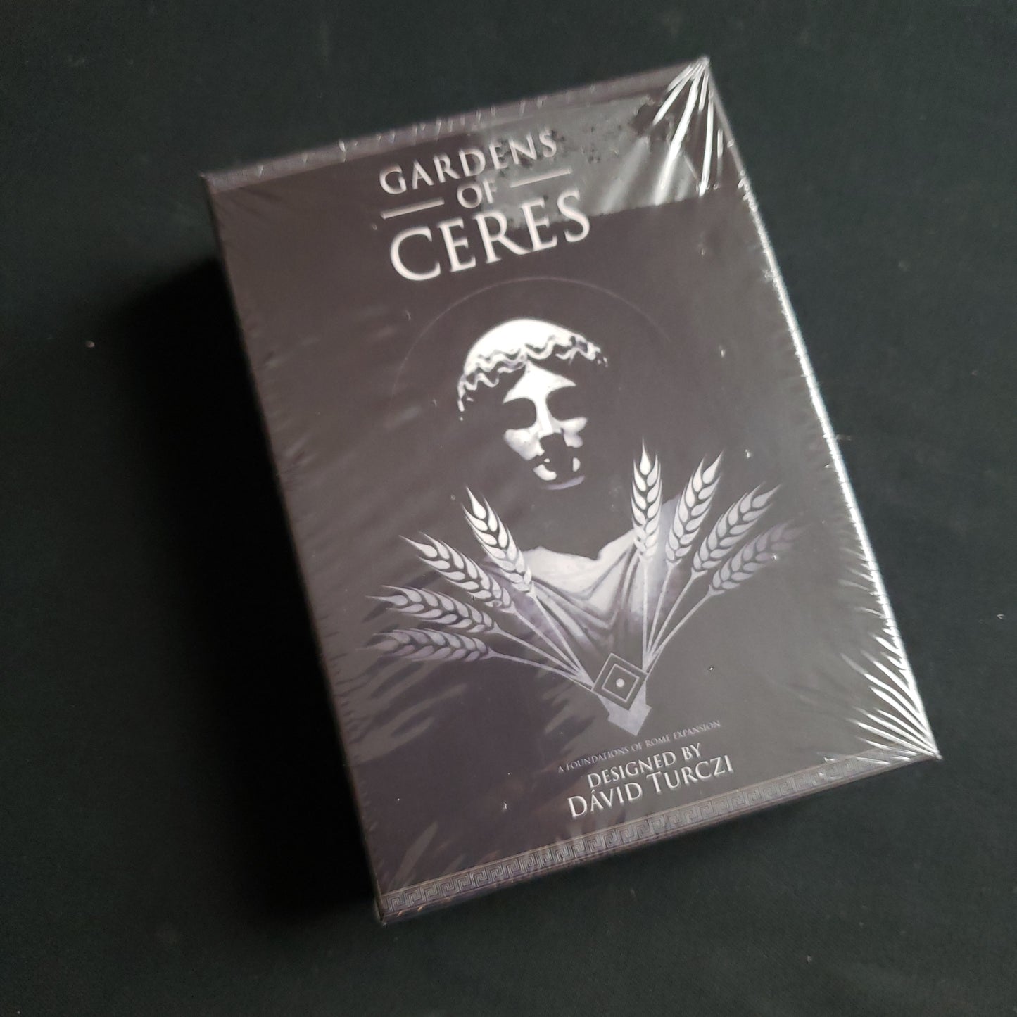 Image shows the front cover of the box of the Gardens of Ceres solo expansion for the board game Foundations of Rome