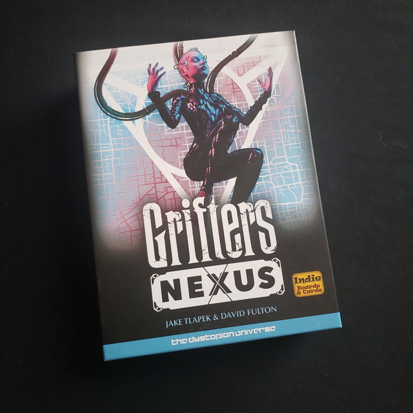 Image shows the front cover of the box of the Grifters: Nexus card game