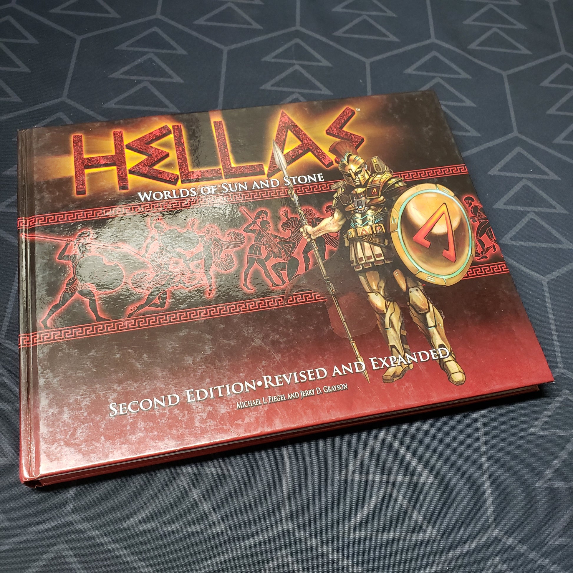 Image shows the front cover of the core rulebook for the roleplaying game HELLAS: Worlds of Sun and Stone