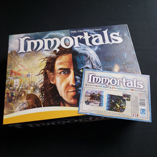 Image shows the front cover of the box of the Immortals board game, along with the instruction sheet for the New Tribes mini expansion sitting on top of it