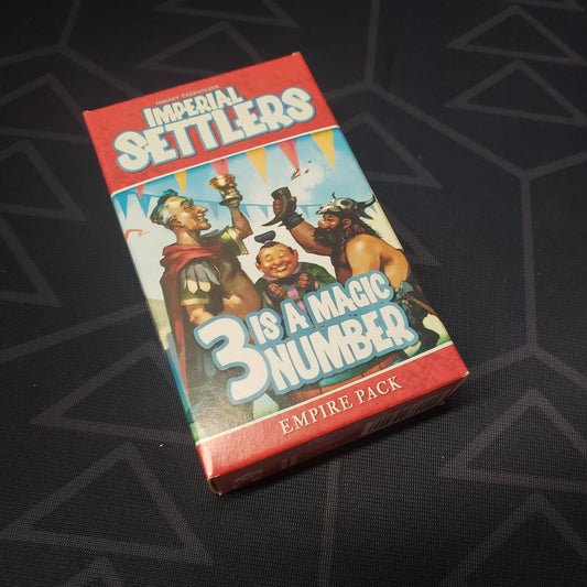 Image shows the front cover of the box of the 3 Is A Magic Number expansion for the card game Imperial Settlers