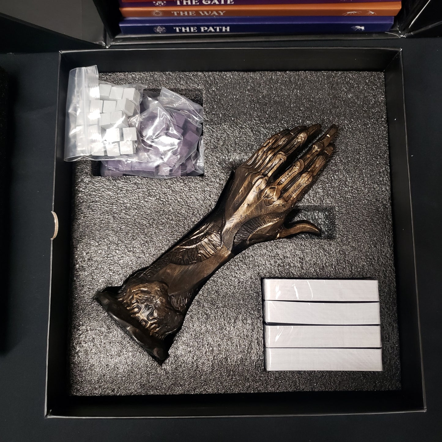 Image shows the metal hand sculpture and sealed cards in the Black Cube for the Invisible Sun roleplaying game