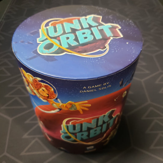Image shows the top and side of the circular box for the Junk Orbit board game