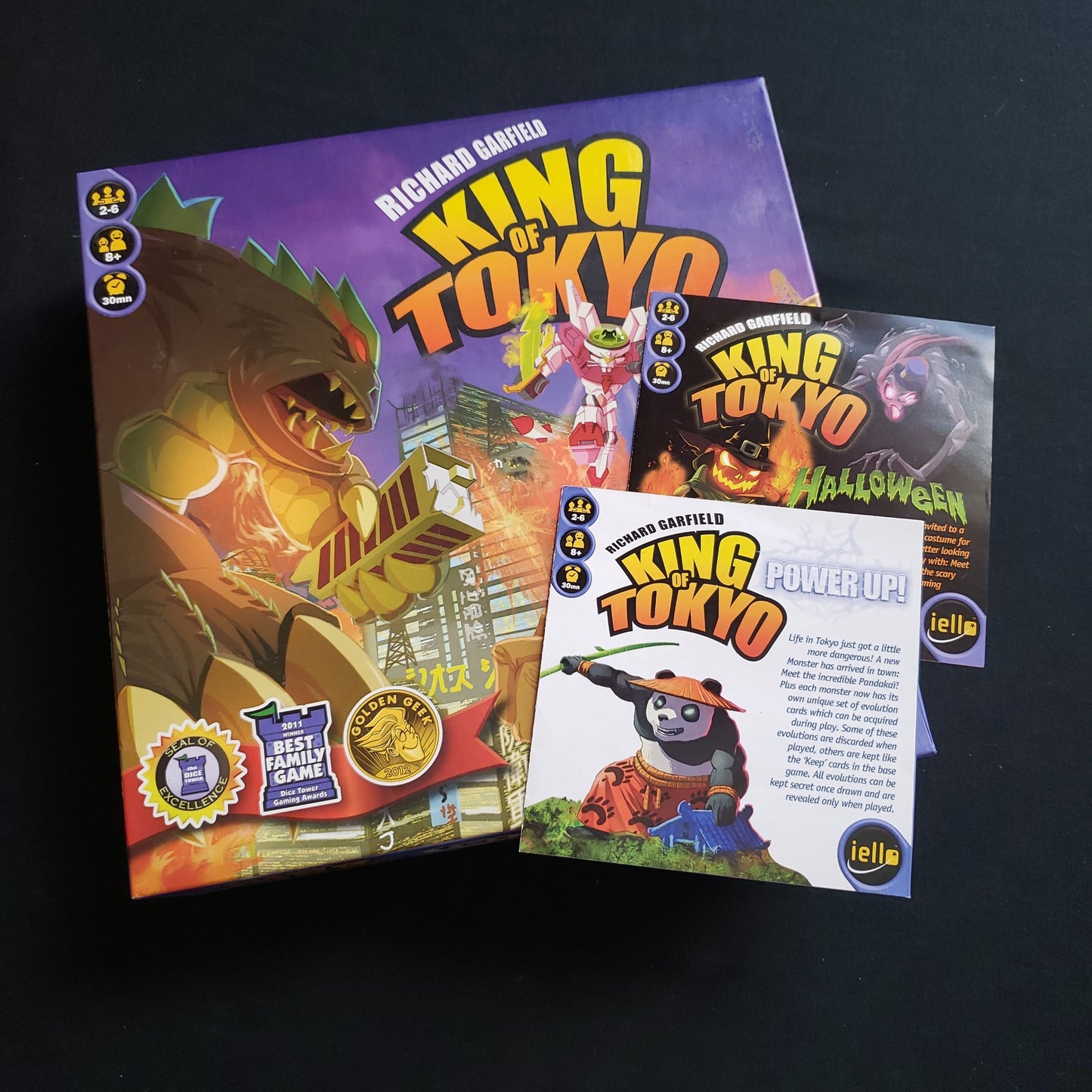 Image shows the front cover of the box of the King of Tokyo board game, with the instructions for the Power Up & Halloween expansions sitting on top of it