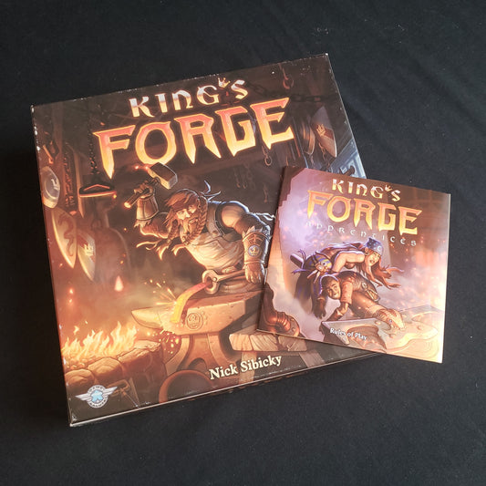 Image shows the front cover of the box of the King's Forge board game, with the instructions for the Apprentices expansion sitting on top of it