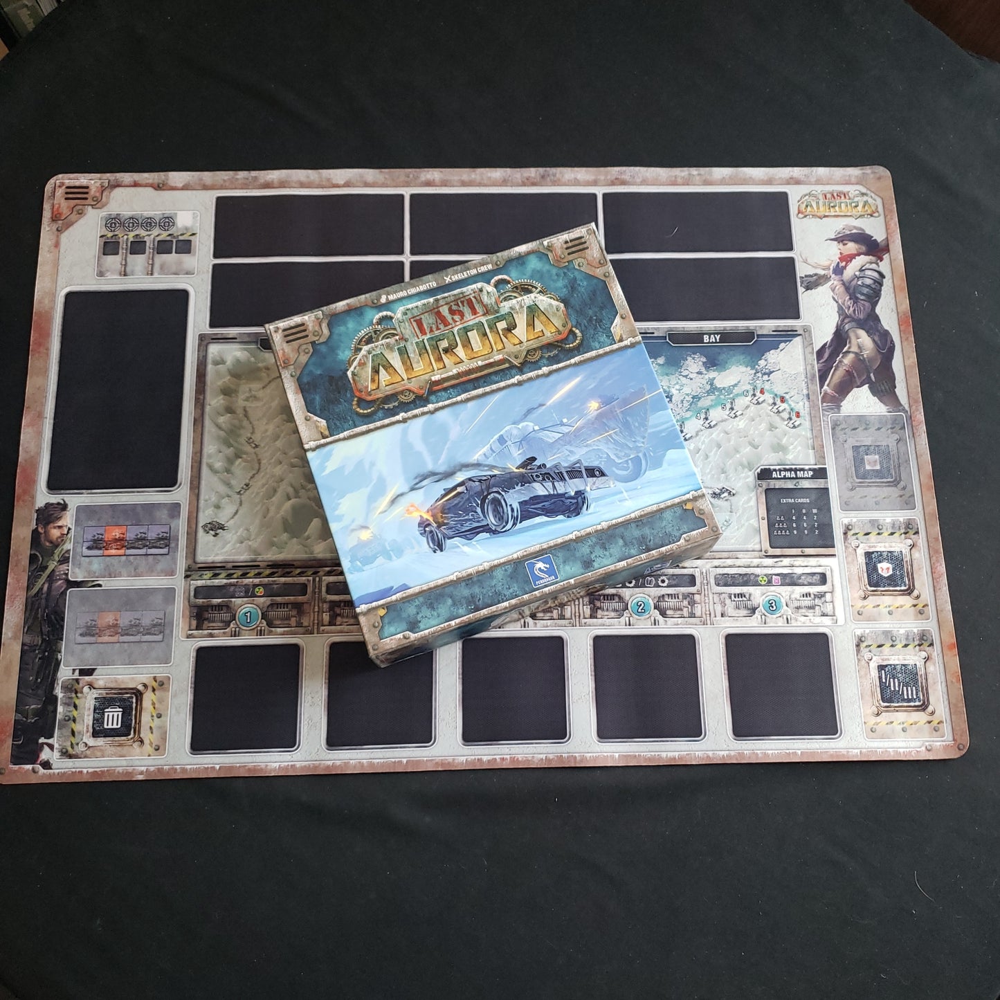 Image shows the box of the Last Aurora board game sitting onto of the neoprene playmat for the game
