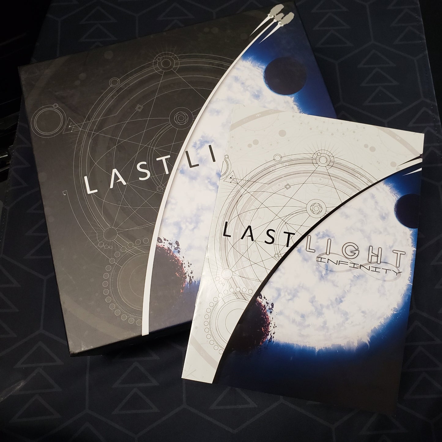 Image shows the front cover of the Deluxe Edition box for the board game Last Light with the instruction manual for the Infinity expansion