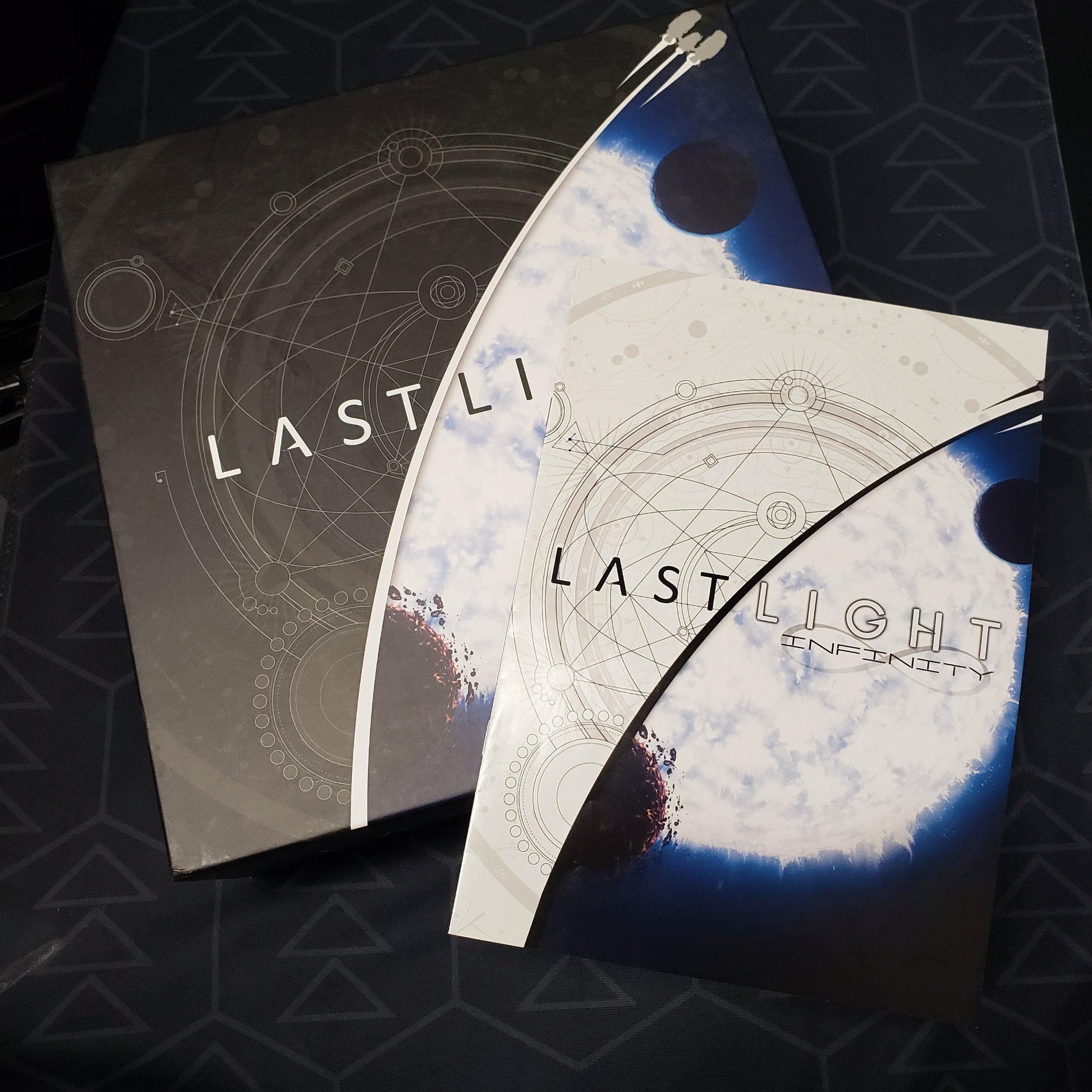 Image shows the front cover of the Deluxe Edition box for the board game Last Light with the instruction manual for the Infinity expansion