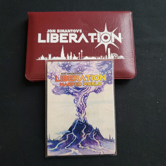 Image shows the front cover of the package for the Liberation card game, with the Warped World expansion sitting on top of it