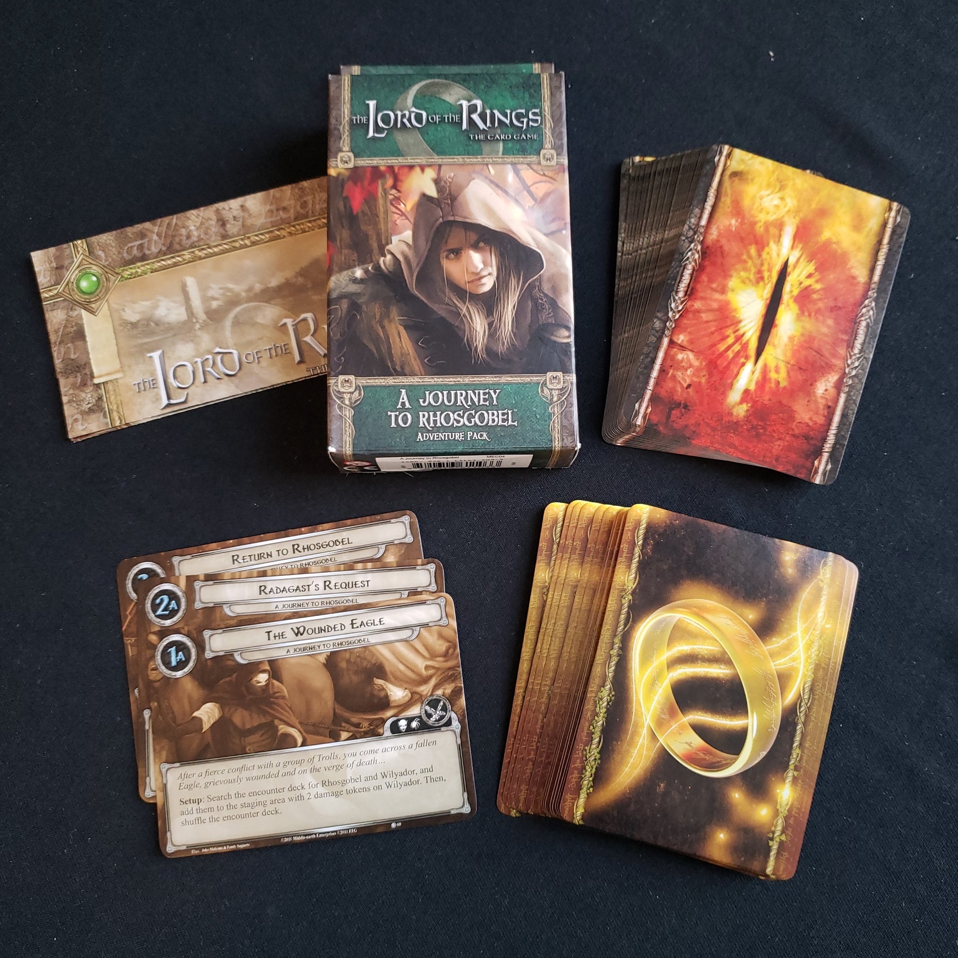 Image shows the front of the package for the Journey to Rhosgobel Adventure Pack for the Lord of the Rings card game, with the cards and instructions fanned out around it