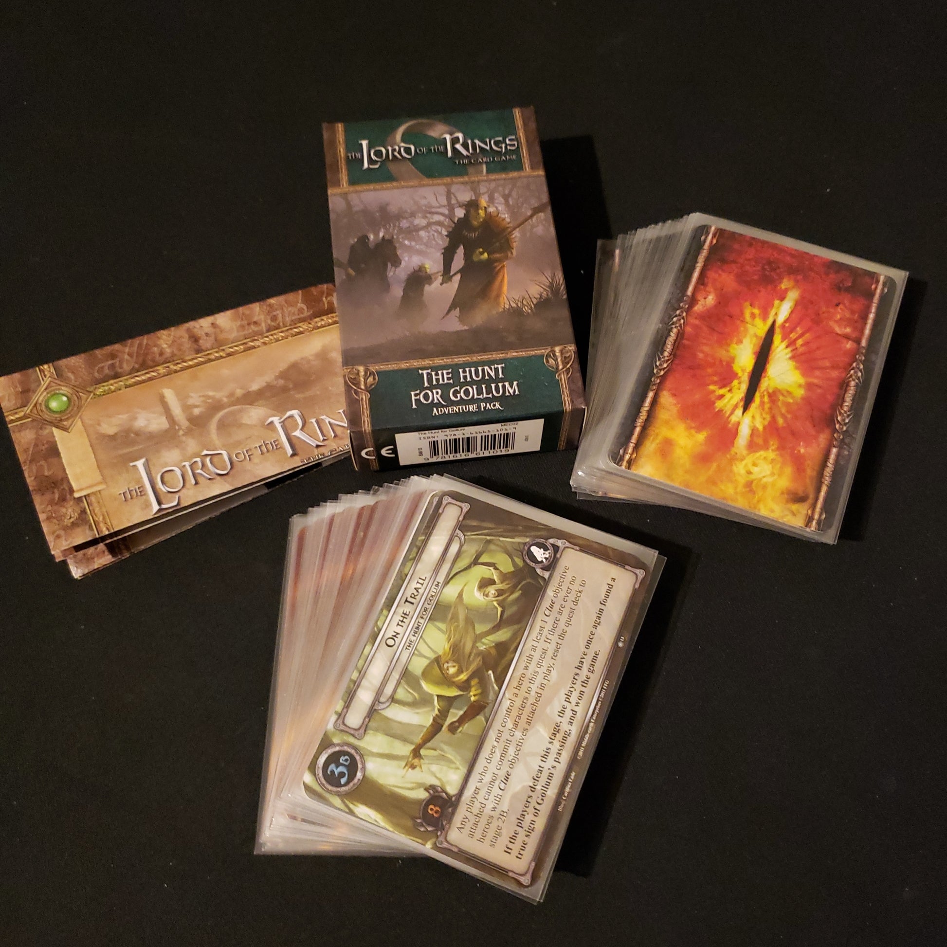 Image shows the front of the package for the Hunt for Gollum Adventure Pack for the Lord of the Rings card game, with the cards and instructions fanned out around it