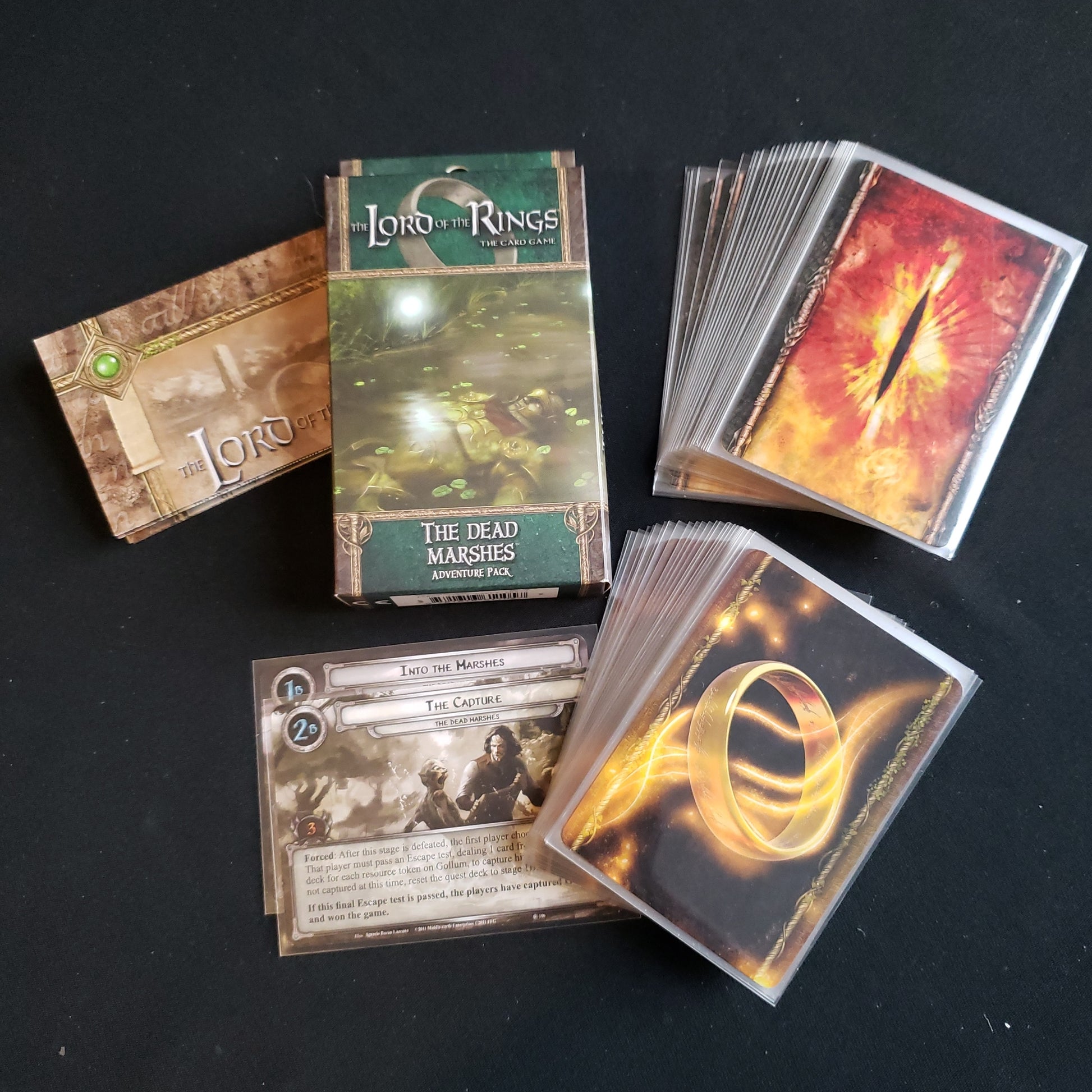 Image shows the front of the package for the Dead Marshes Adventure Pack for the Lord of the Rings card game, with the cards and instructions fanned out around it